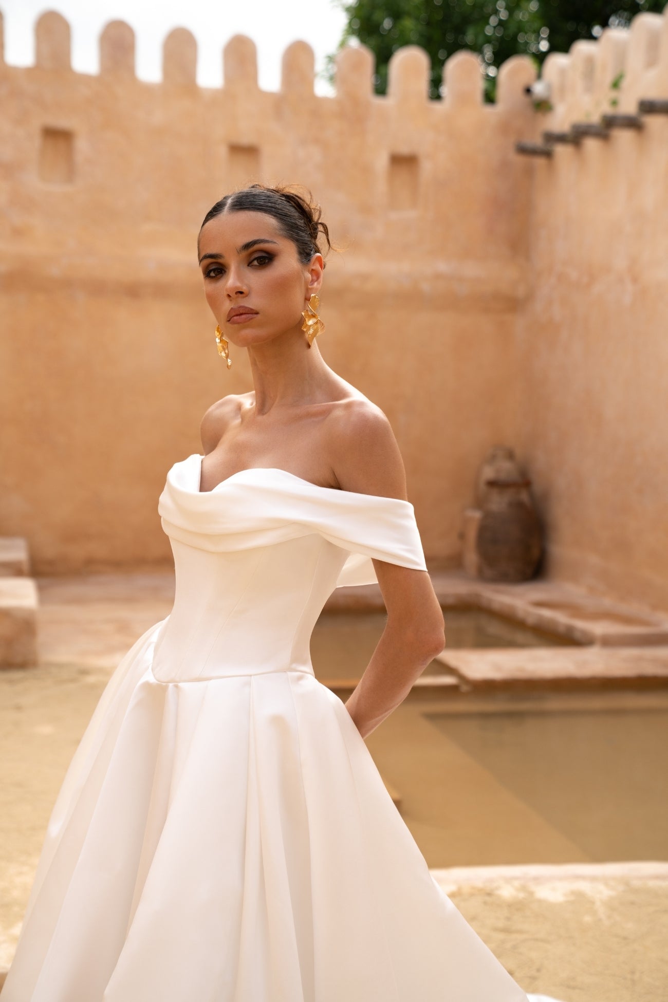A line wedding gown featuring off the shoulder straps and a sweetheart neckline, in a minmal plain fabric, high split and dramatic skirt.