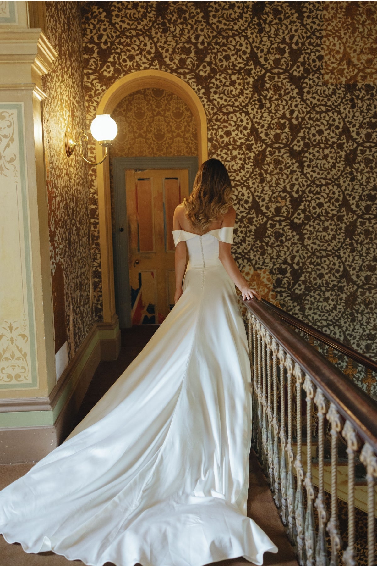 A satin sheath fit wedding gown featuring off the shoulder neckline and cap sleeves.