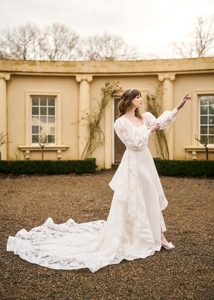 Model wears Tamia overskirt. Double layered detachable overskirt made from floral organza with waterfall train.