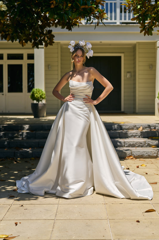 Bride wears Lisha gown with voluminous Lisha Overskirt made from ivory Mikado fabric. Overskirt drops from side seam to side seam, trailing behind. 
