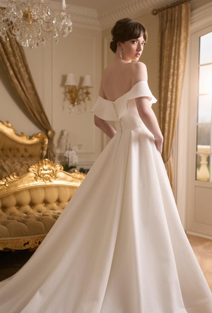 Back view of Tyler Dress showing off-the-shoulder flared band joining at the centre of the back. Covered buttons run to bottom of zip. Voluminous a-line skirt and train.