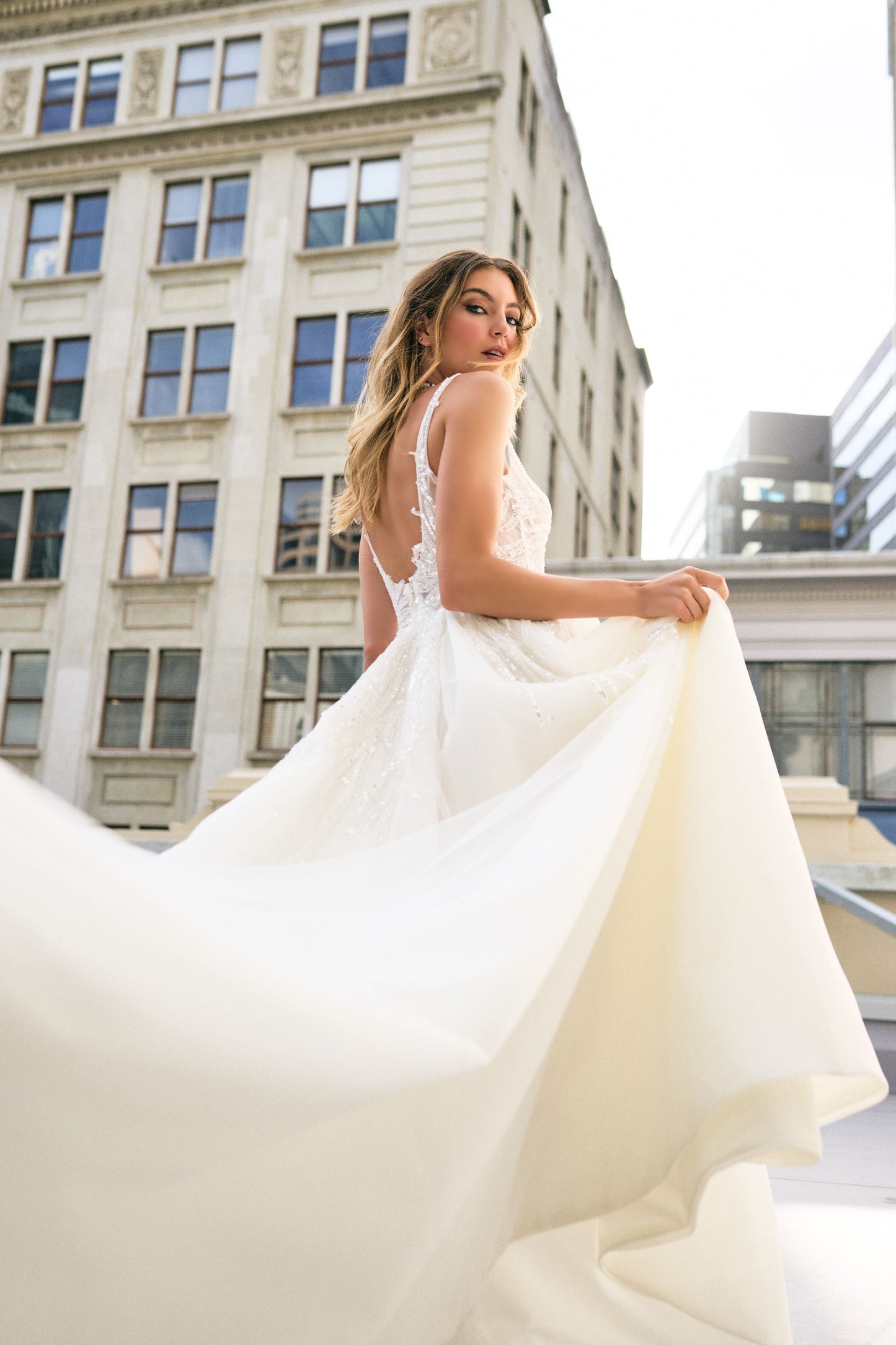 Raffael wedding dress from Jessica Coutures. Square neckline, low back A-line dress with organza fabric and glitter detailing at the bodice. Boning support, cinched waist, dramatic skirt. Hidden features include pockets and a split for easy movement.