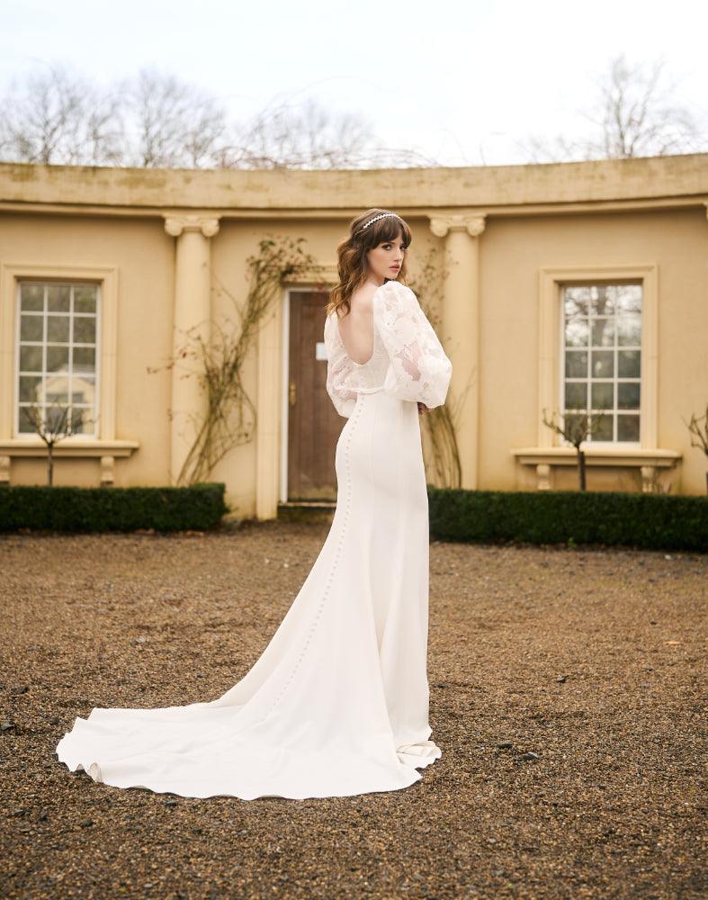 Tamia gown back view. Scoop back with covered buttons that run the length of the train. Floral organza balloon sleeves featured.