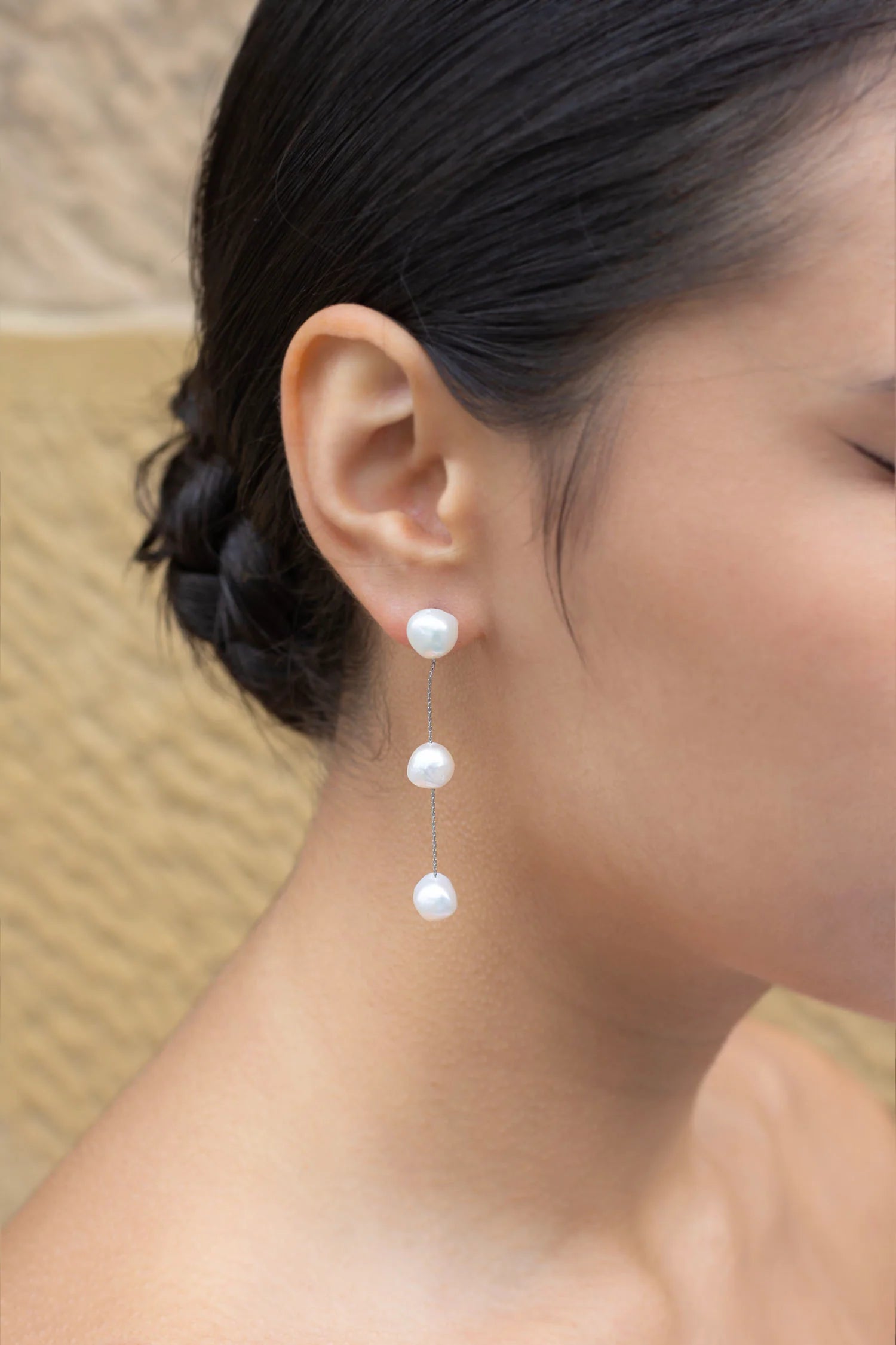 Image of model wearing earring with three freshwater pearls hanging in a row joined by silver chain.