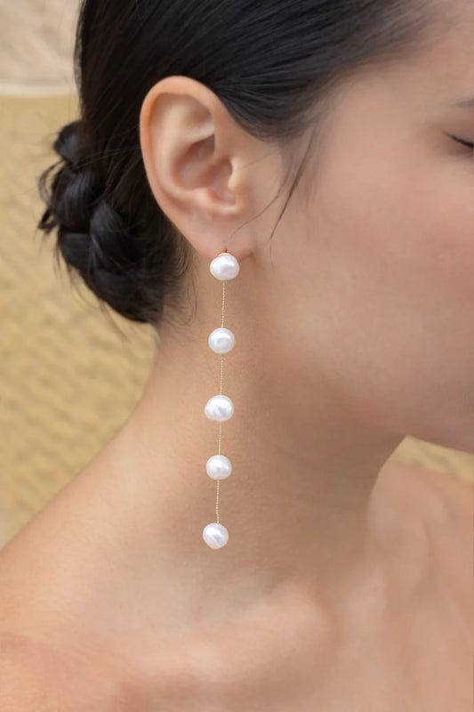 Image of model wearing earring with five freshwater pearls hanging in a row joined by gold chain.