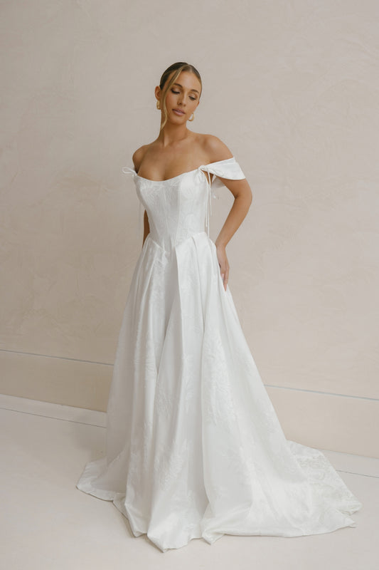 A-line wedding gown in Floral Jacquard fabric, off-the-shoulder sleeves, pleated skirt. 