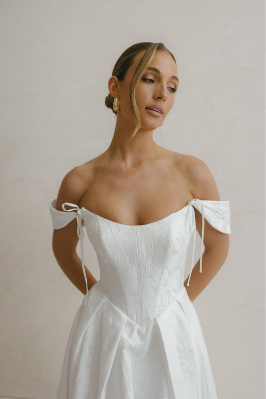A-line wedding gown in Floral Jacquard fabric, off-the-shoulder sleeves, pleated skirt. 