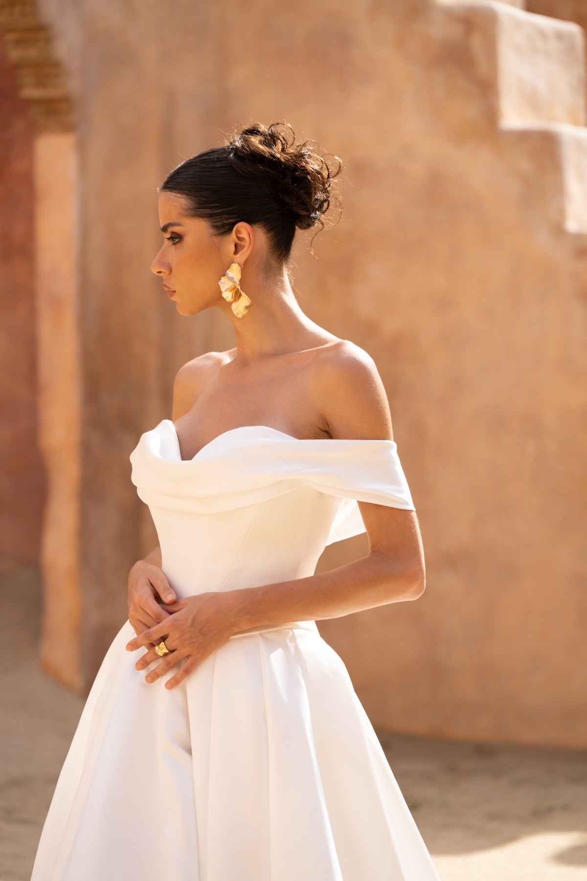 A line wedding gown featuring off the shoulder straps and a sweetheart neckline, in a minmal plain fabric, high split and dramatic skirt. 