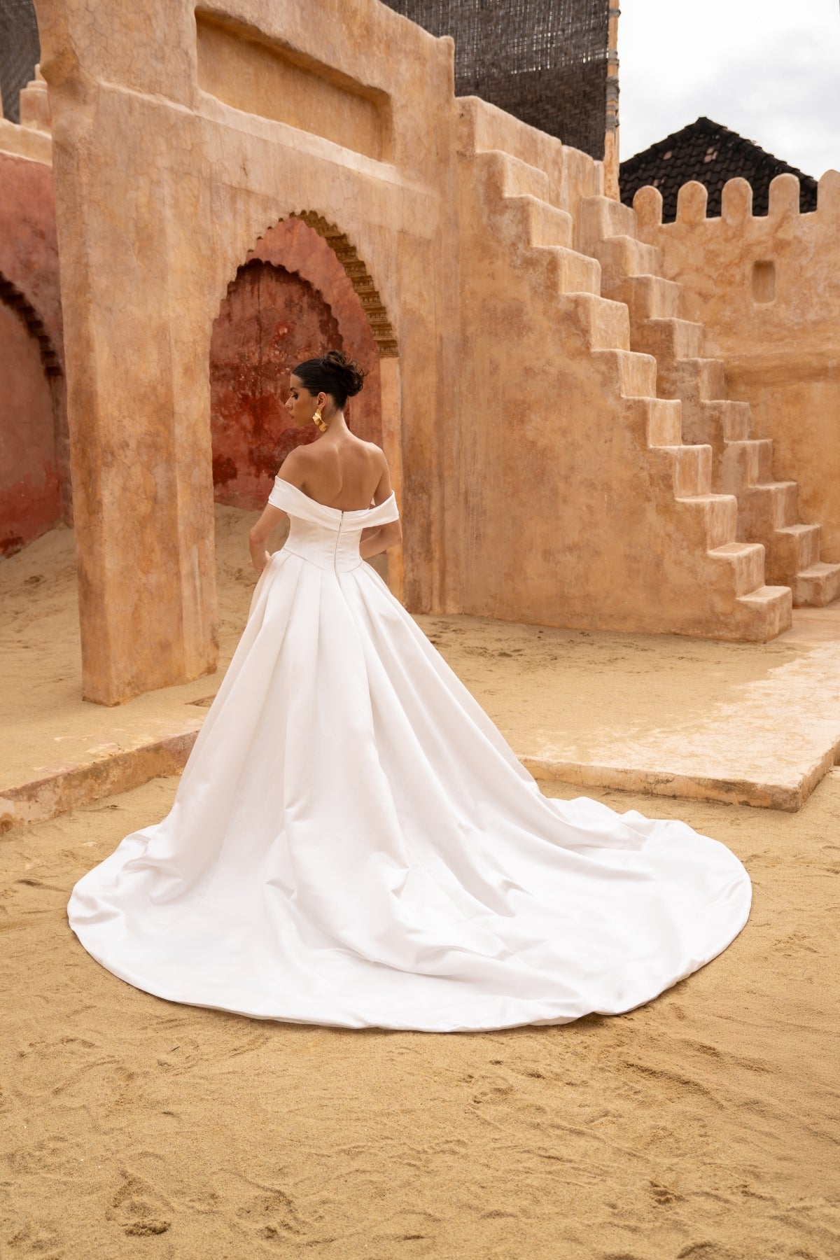 A line wedding gown featuring off the shoulder straps and a sweetheart neckline, in a minmal plain fabric, high split and dramatic skirt. 