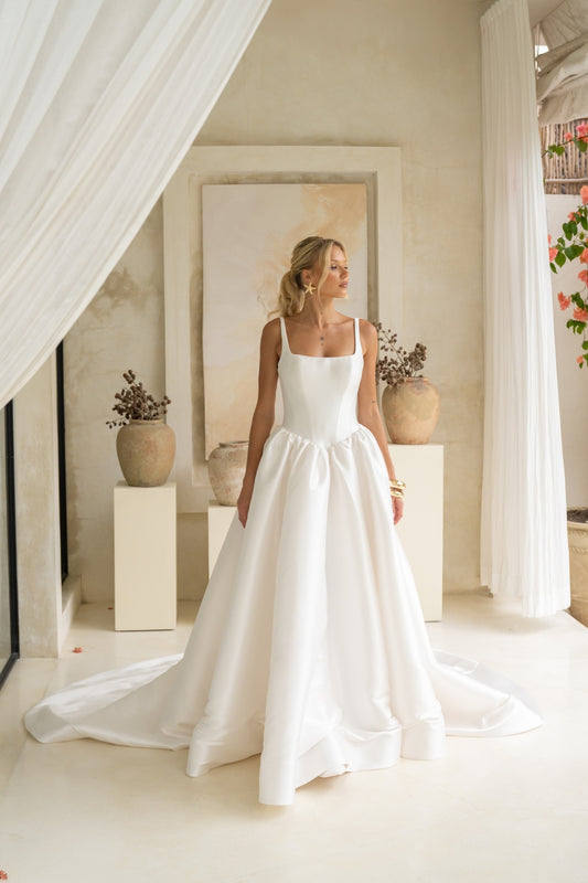 Dramatic A-line wedding gown featuring a squared neckline with straps. subtle basque waist with ruching all around waistline. chapel train. 