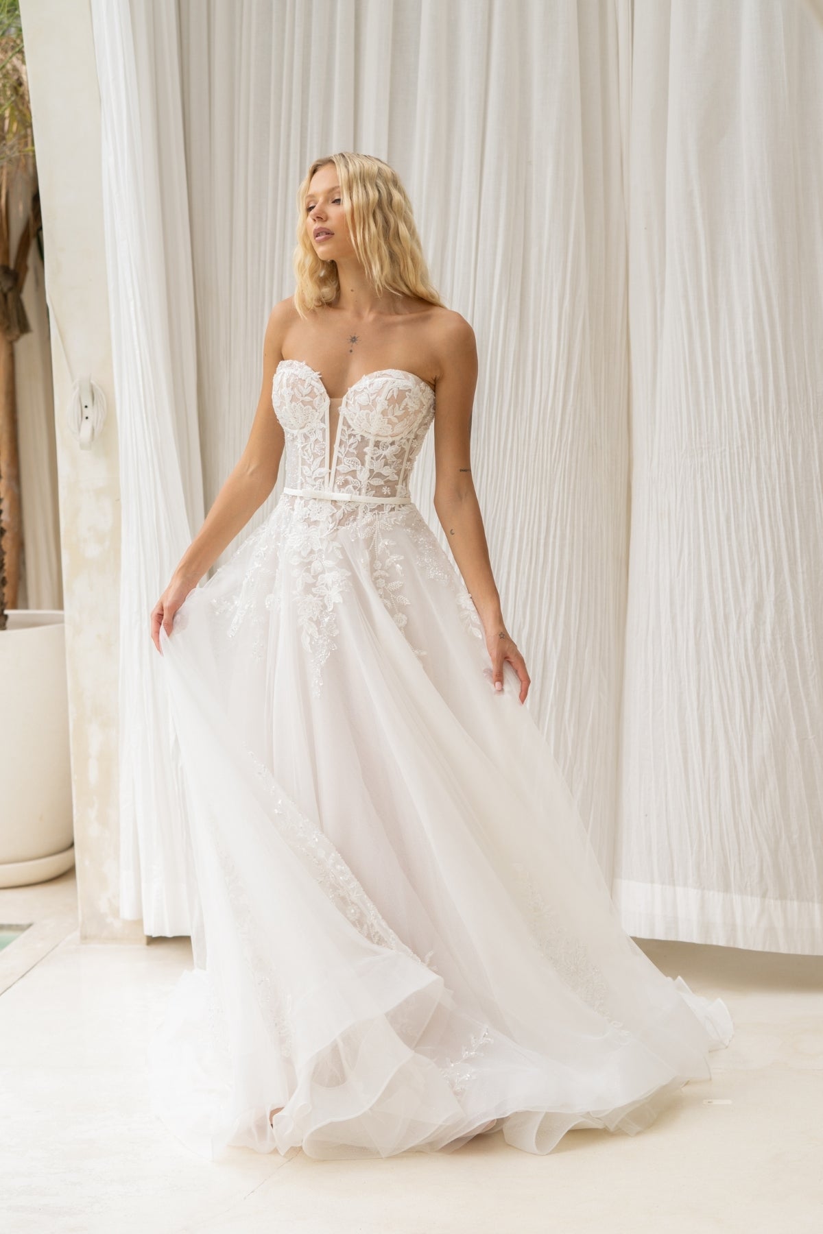 A-line wedding dress with v-plunge sweetheart neckline, floral lace, waistbelt and subtle basque waist, flowing tulle skirt. 