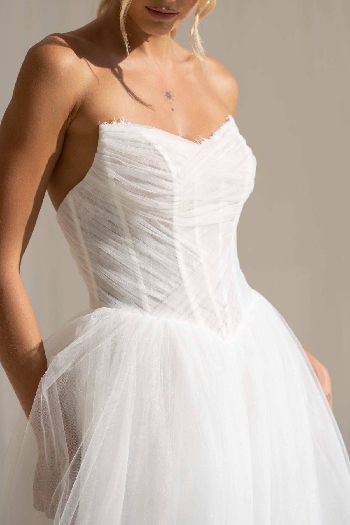 A-line wedding gown with cat-eye strapless neckline, criss cross ruching around the bust, corset boning on the bodice, basque waist and a voluminous tulle skirt. 