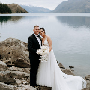 Bride and groom smile in front of lake and mountains.