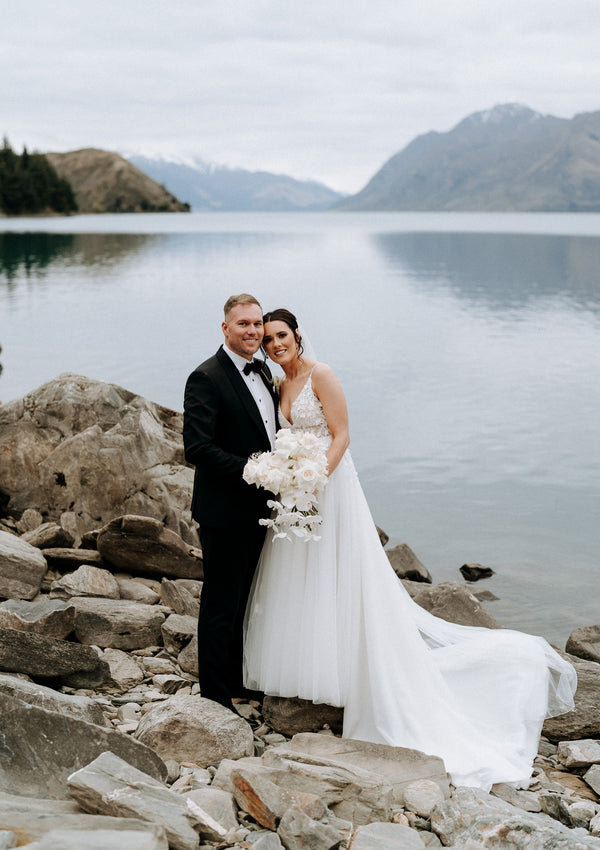 Bride and groom smile in front of lake and mountains.