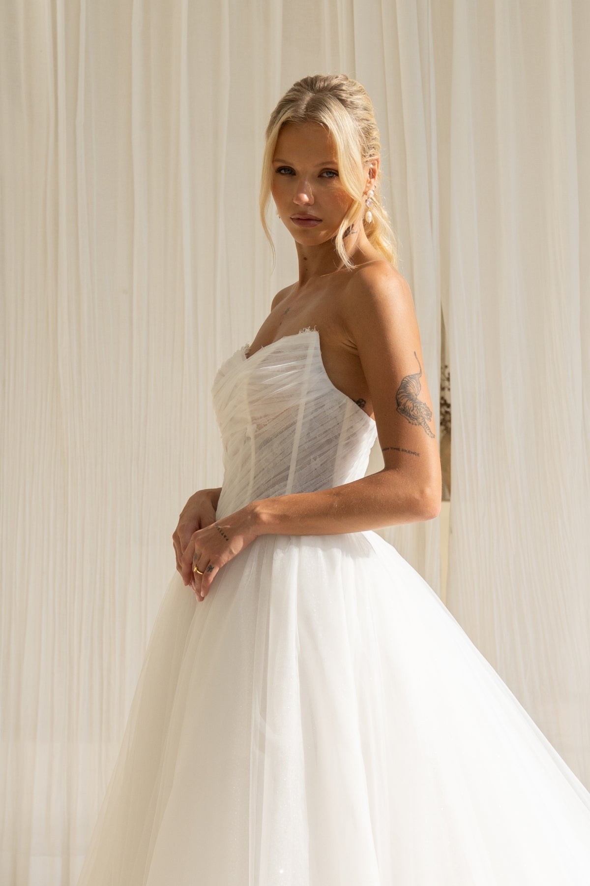 A-line wedding gown with cat-eye strapless neckline, criss cross ruching around the bust, corset boning on the bodice, basque waist and a voluminous tulle skirt. 
