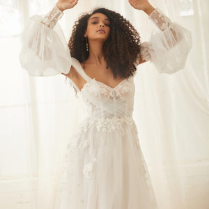 Mid shot of model wearing sky sleeves. Detachable sleeves made from soft tulle in a balloon shape. They sit on upper arm and have floral cuffs.'