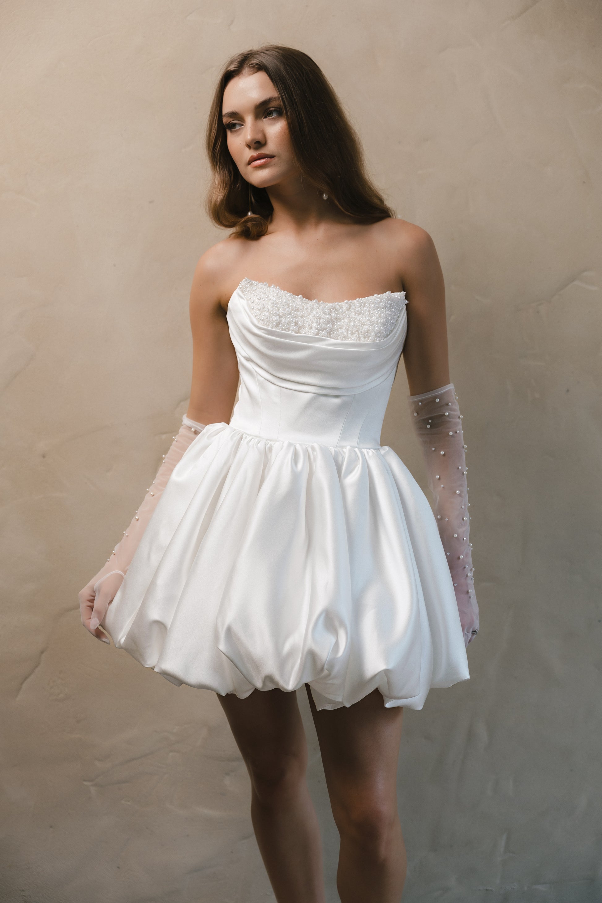 Bridal gown Brittany features a pearl-encrusted corset bodice, ruffled bubble skirt, and underbust ruching for a flattering lift. Designed for the chic, fashion-forward bride by Roselle Collection Jessica Couture.