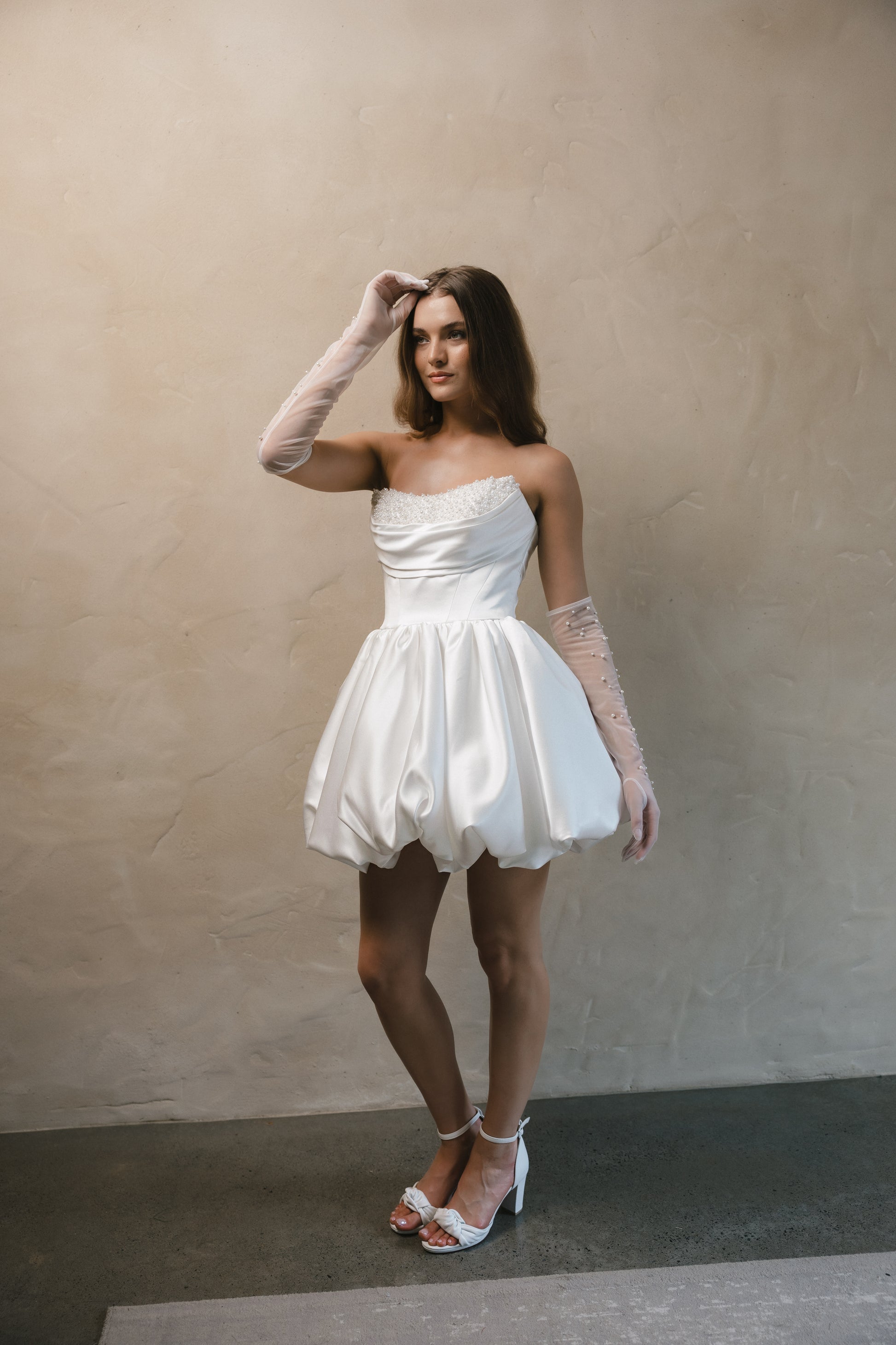 Bridal gown Brittany features a pearl-encrusted corset bodice, ruffled bubble skirt, and underbust ruching for a flattering lift. Designed for the chic, fashion-forward bride by Roselle Collection Jessica Couture.