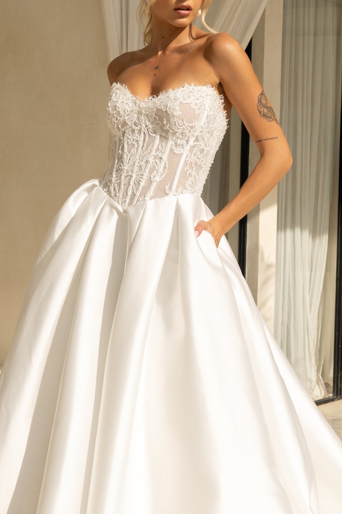 A-line wedding dress with a strapless sweetheart bodice covered in lace and corset boning, basque waistline, and a voluminous dramatic skirt in plain fabric. 