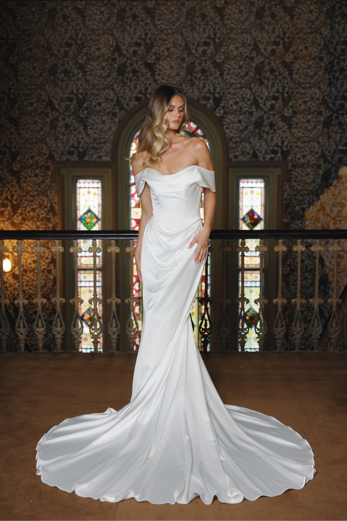 A satin sheath fit wedding gown featuring off the shoulder neckline and cap sleeves. 