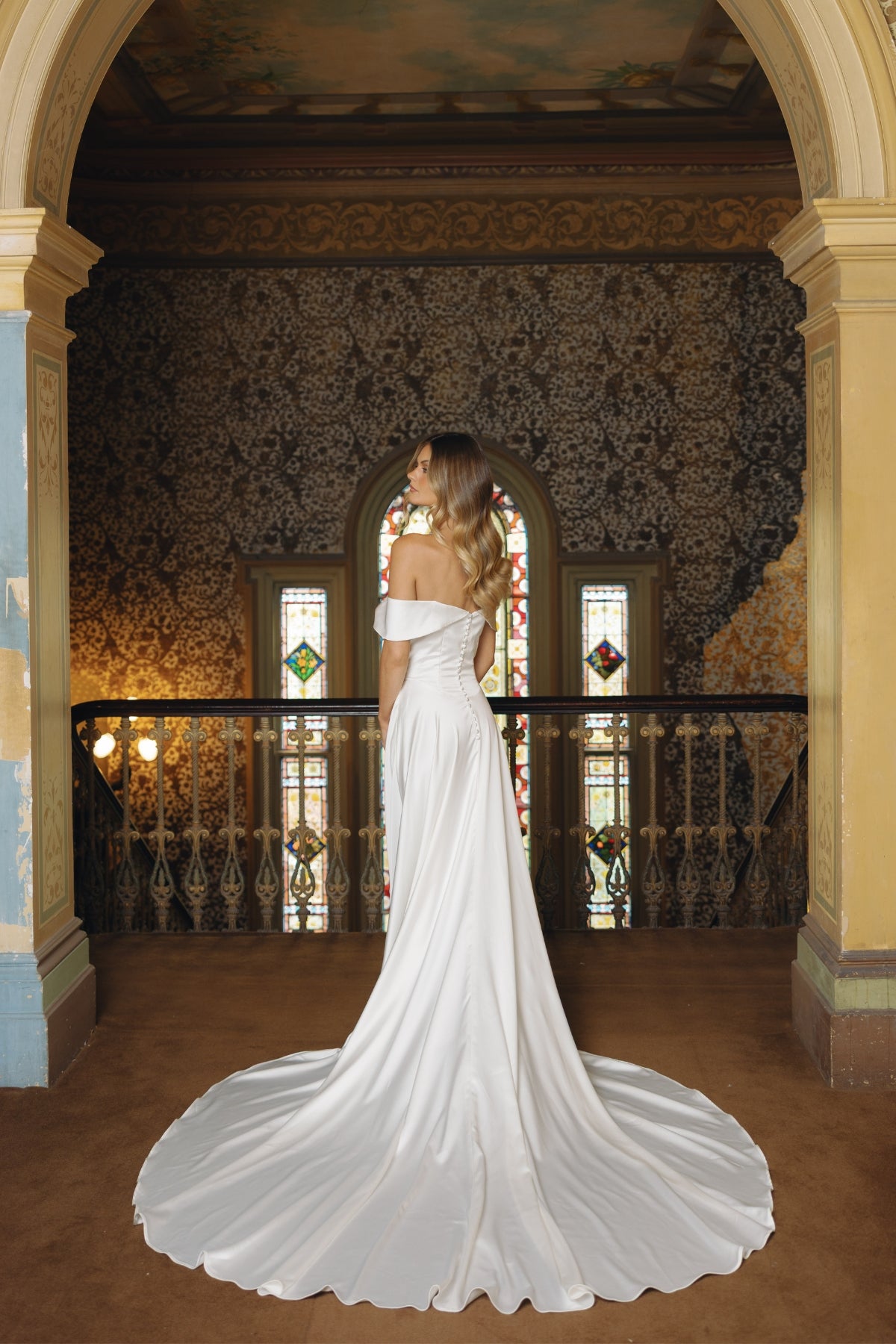 A satin sheath fit wedding gown featuring off the shoulder neckline and cap sleeves. 