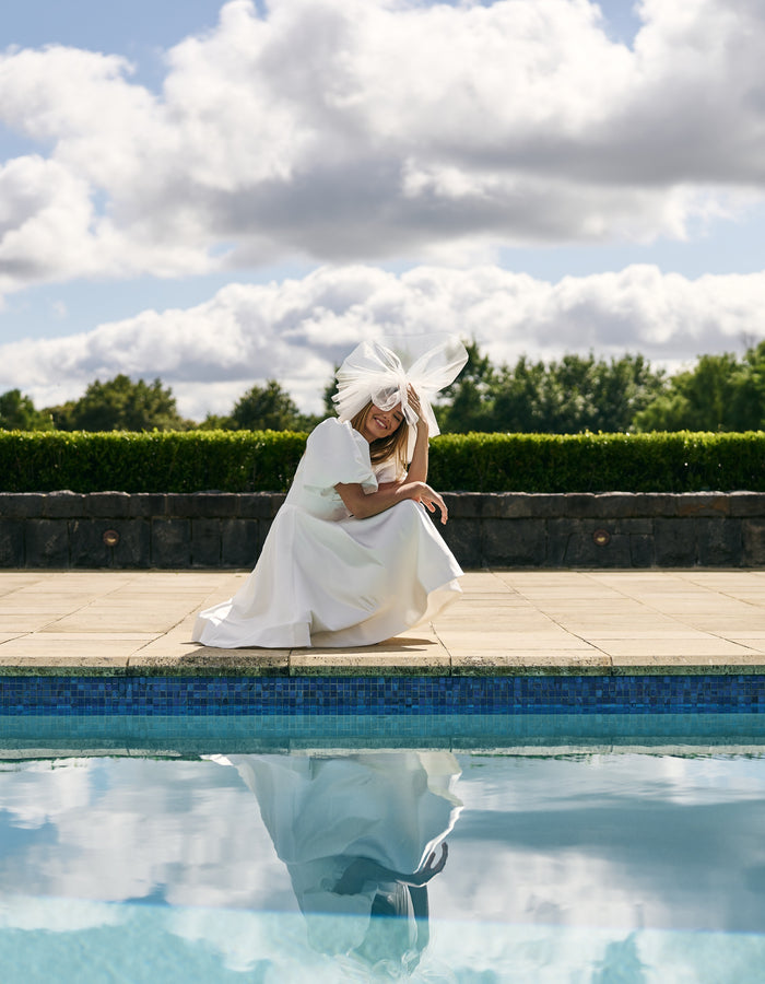 Bride kneels next to pool in short stiff tulle veil