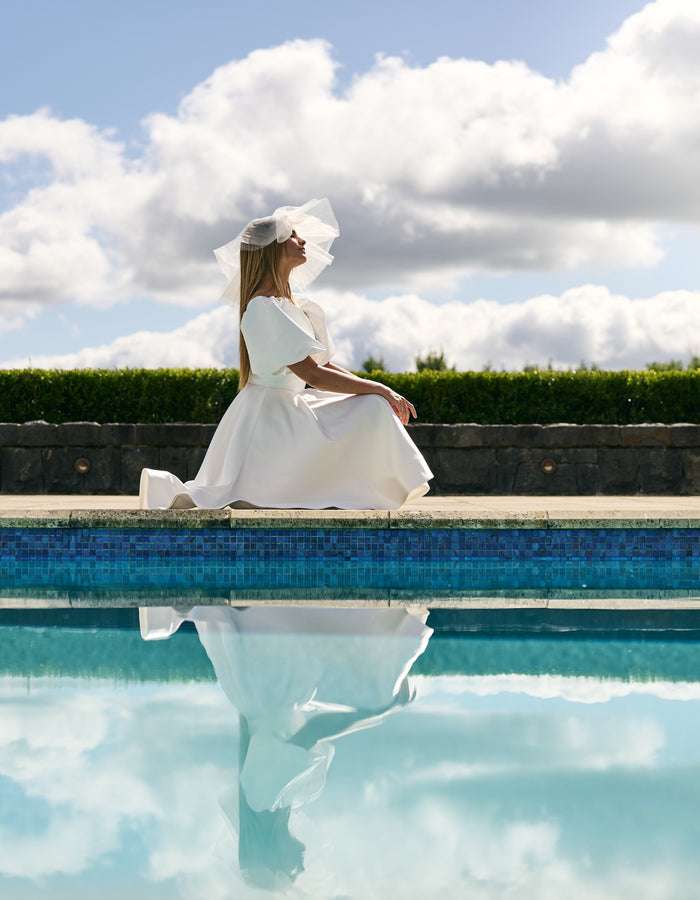 Bride kneels next to pool on short stiff tulle veil