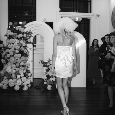 Black and white image of ivory satin mini dress shown from the back with waist bow