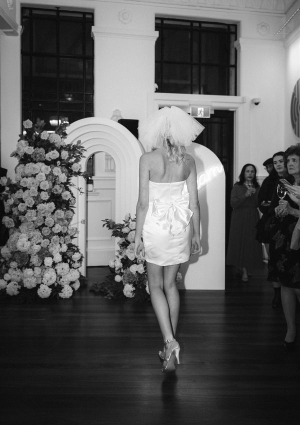 Black and white image of ivory satin mini dress shown from the back with waist bow
