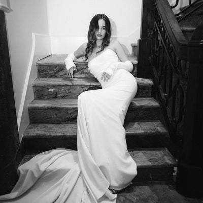 Model sits on stairs in strapless Tina gown and separate ivory mikado sleeves