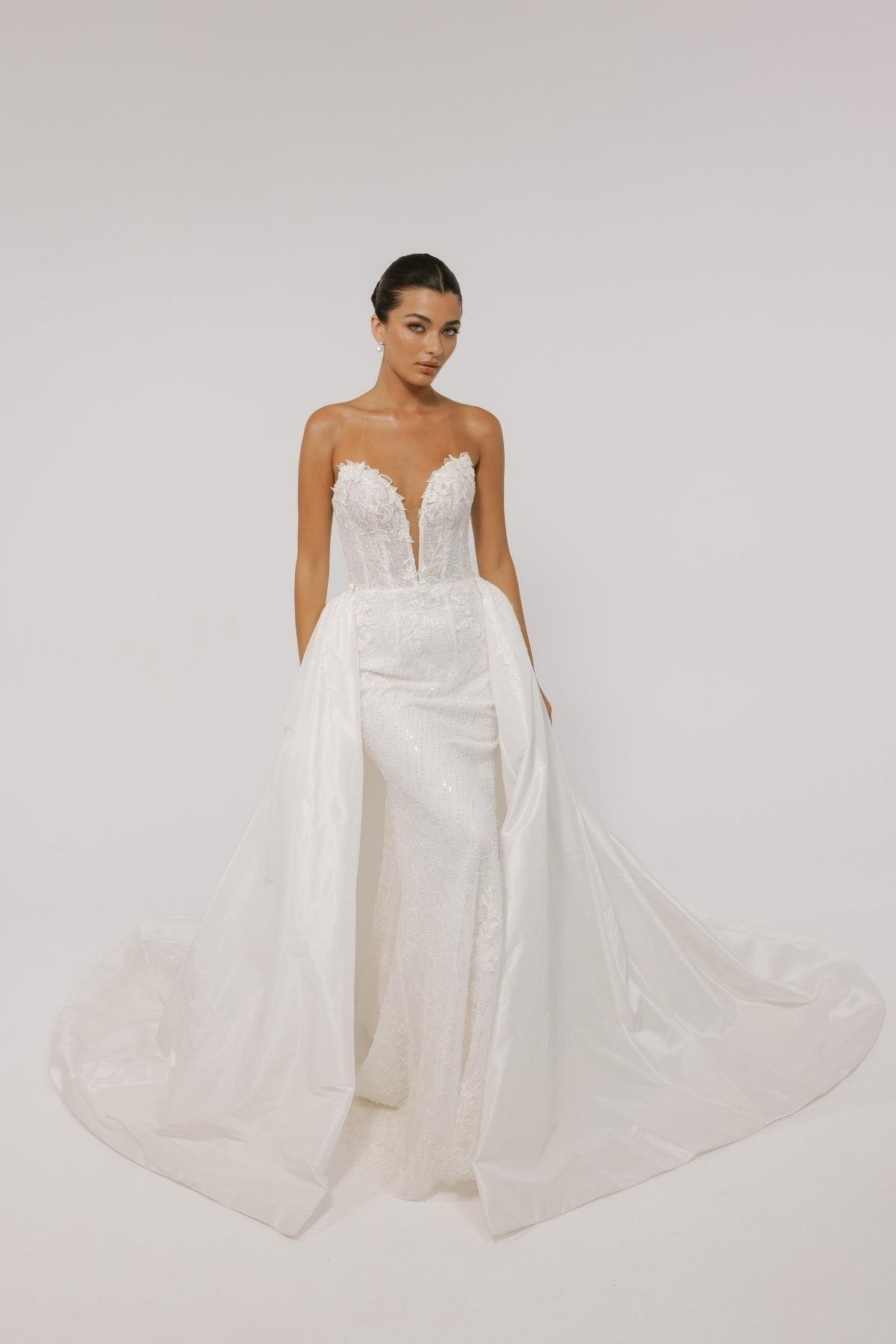 Fitted wedding gown with a deep v plunge, strapless neckline, beaded lace. With voluminous overskirt 
