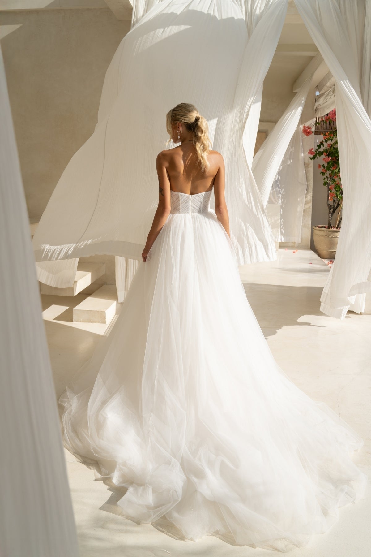 A-line wedding gown with cat-eye strapless neckline, criss cross ruching around the bust, corset boning on the bodice, basque waist and a voluminous tulle skirt. 