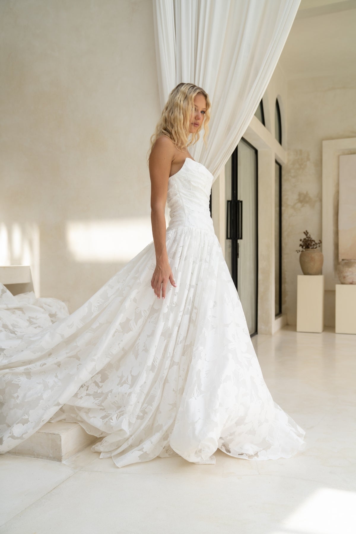A-line drapy wedding gown featuring a cat-eye neckline, corseted bodice, and floral jacquard fabric. 