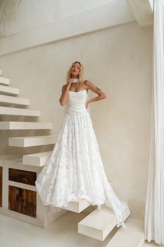 A-line drapy wedding gown featuring a cat-eye neckline, corseted bodice, and floral jacquard fabric. 