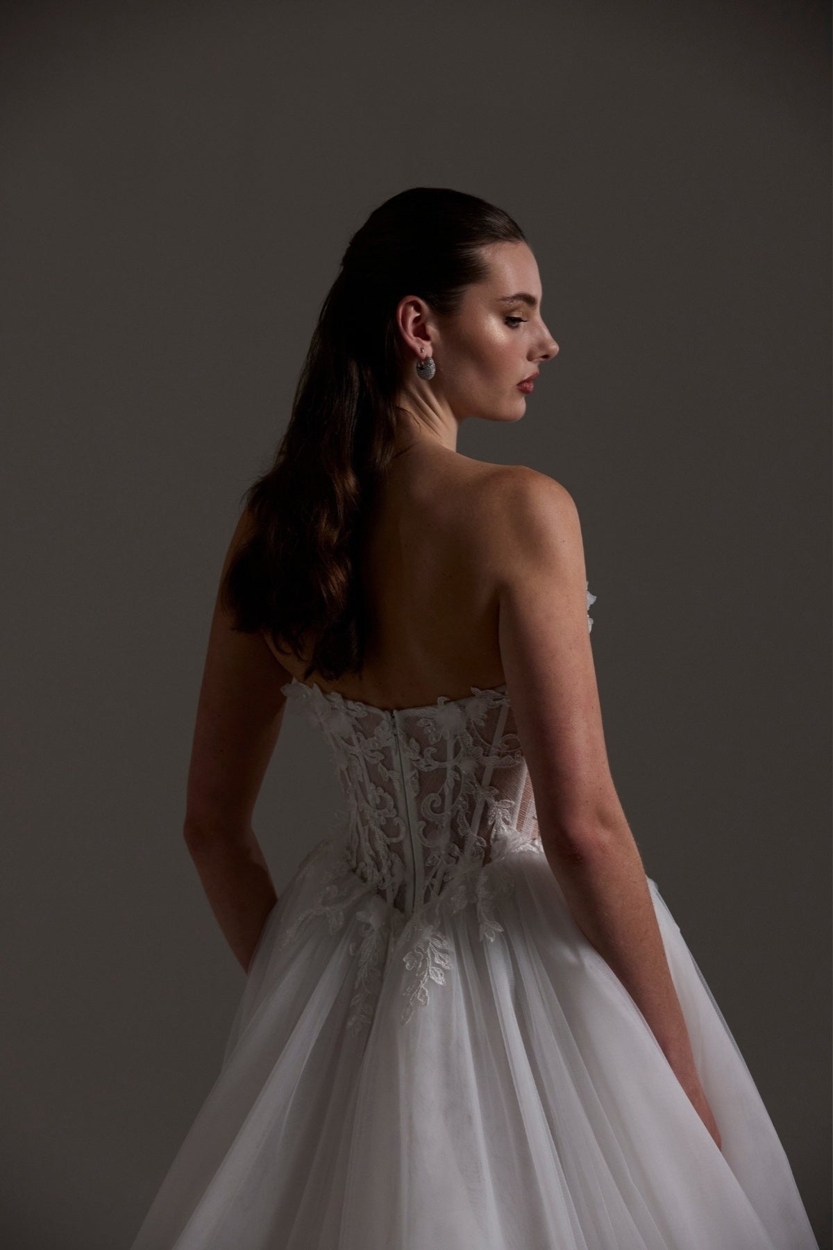 A-line Wedding dress featuring a tulle skirt, lace corseted bodice with basque waistline, cat-eye neckline, and buttons down the front of bodice. 