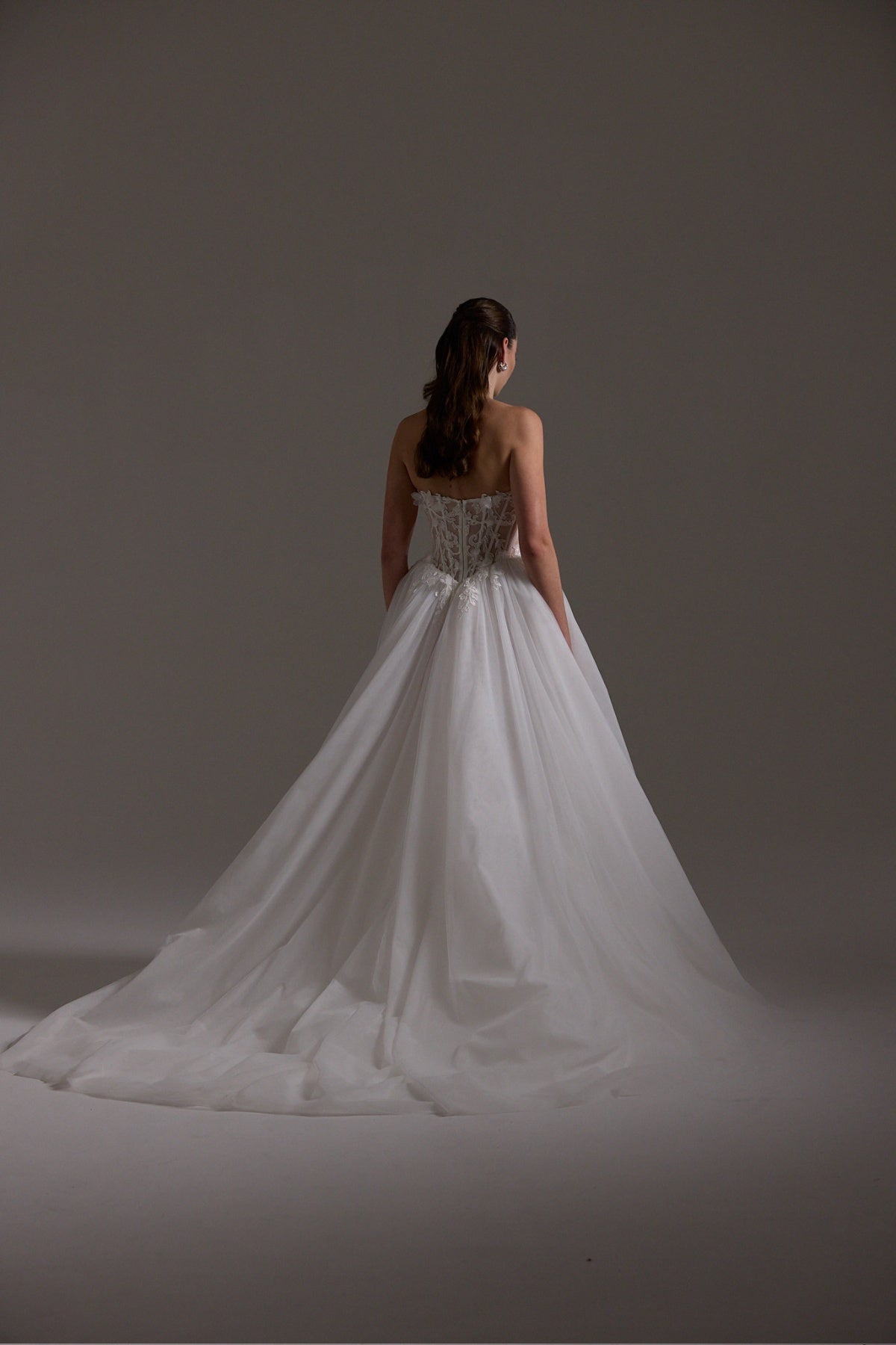A-line Wedding dress featuring a tulle skirt, lace corseted bodice with basque waistline, cat-eye neckline, and buttons down the front of bodice. 