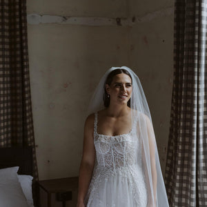 Bride stands next to bed in Lotter Dress and Pippa Veil with beaded border.