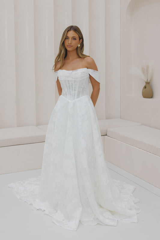 A-line wedding gown with off the shoulder neckline, ruched bust, and jacquard organza fabric. 