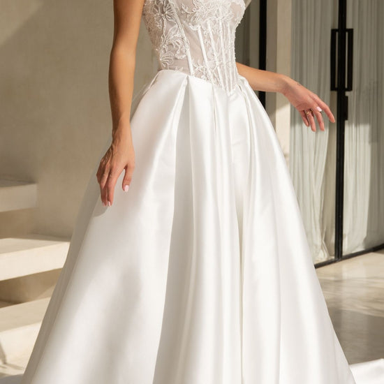 A-line wedding dress with a strapless sweetheart bodice covered in lace and corset boning, basque waistline, and a voluminous dramatic skirt in plain fabric. 