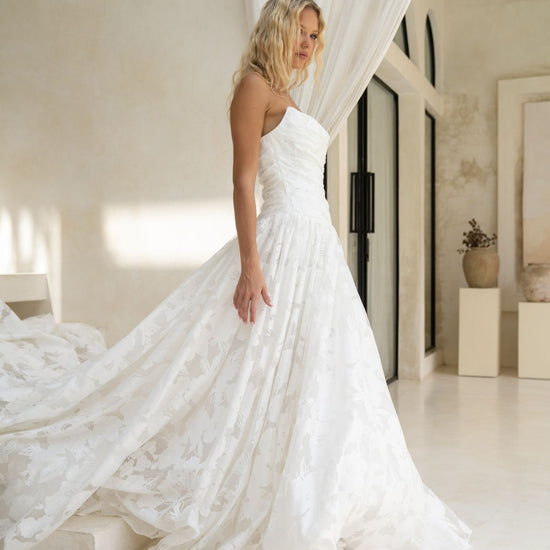 A-line drapy wedding gown featuring a cat-eye neckline, corseted bodice, and floral jacquard fabric. 