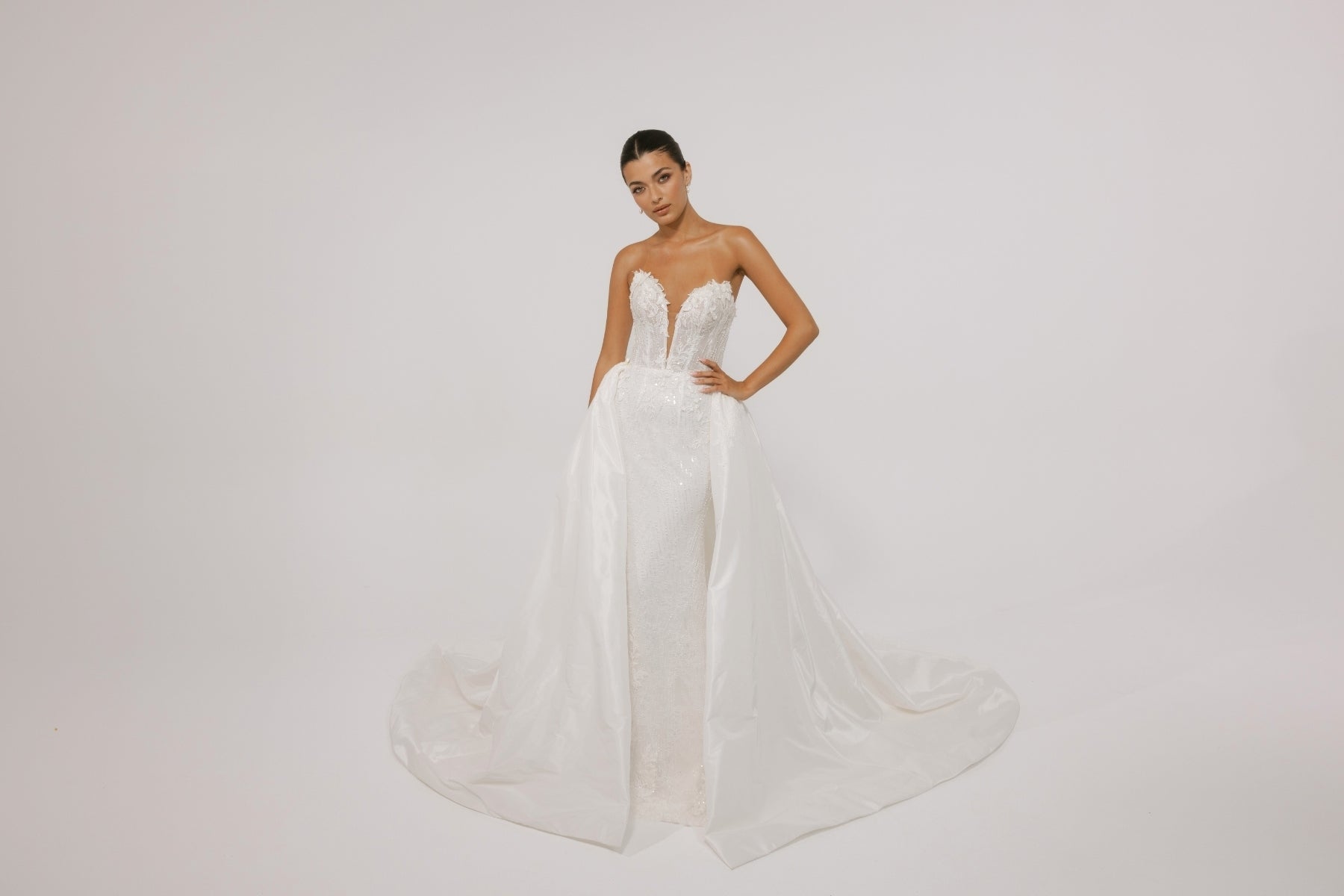 Fitted wedding gown with a deep v plunge, strapless neckline, beaded lace. With voluminous overskirt 
