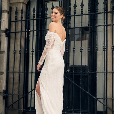 Fully beaded off the shoulder gown with sheer sleeves. Fit-n-flare silhouette, bust rouching and boned bodice. Back view of gentle V-neckline.