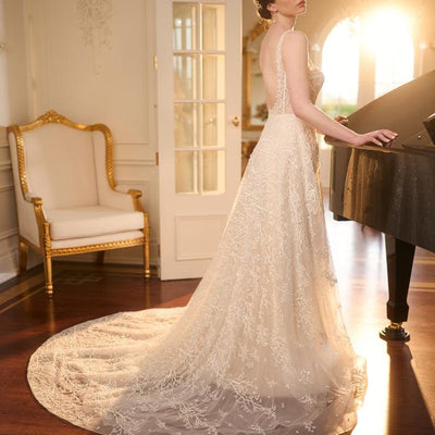 Side view, plunging curved back with embroidered train. Ivory Bridal gown with sheer lace embroidered with beaded branches. Square neckline with thin straps and a-line skirt.