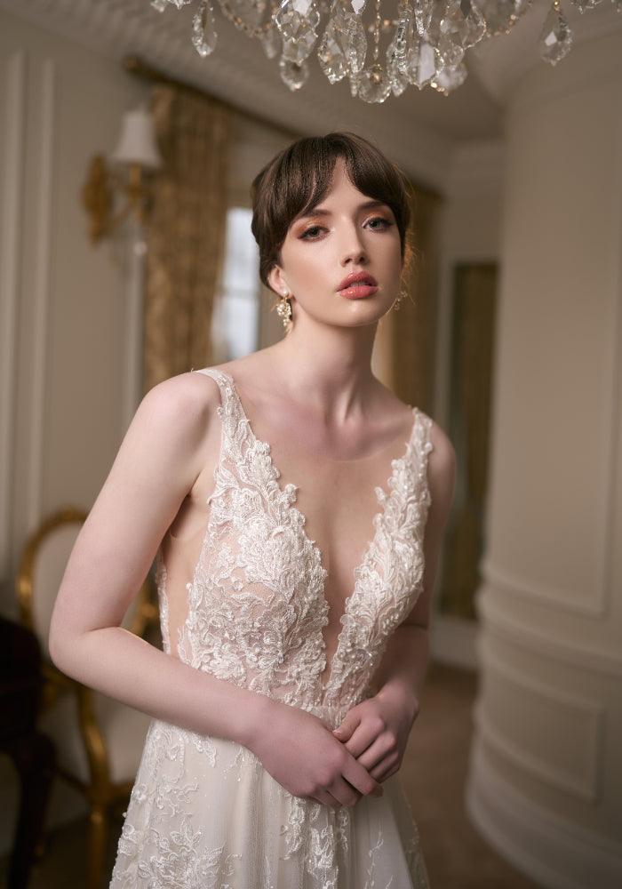 Close up of wedding gown bodice. Plunging V-neckline, illusion mesh with lace applique framing the bodice. Embroidered with pearls and beads.