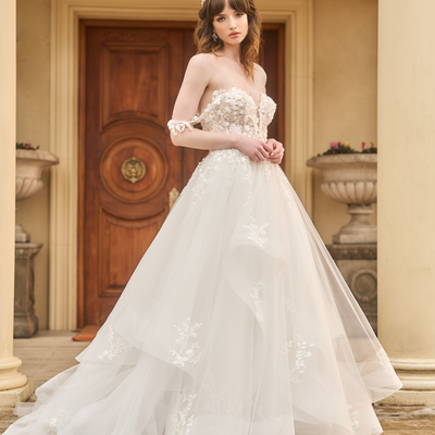 Tess is an a-line wedding gown with plunging sweetheart neckline. Asymmetrical voluminous tulle skirt with subtle structure in hem. Delicate floral off-the-shoulder straps match the lace bodice and applique on skirt.