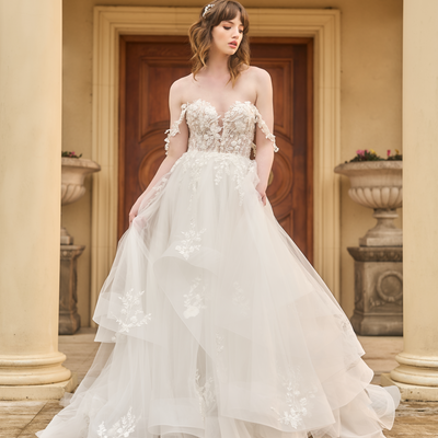 Tess is an a-line wedding gown with plunging sweetheart neckline. Asymmetrical voluminous tulle skirt with subtle structure in hem. Delicate floral off-the-shoulder straps match the lace bodice and applique on skirt.