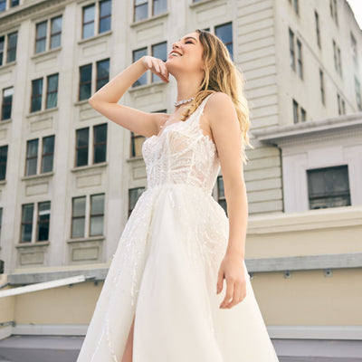 Raffael wedding dress from Jessica Coutures. Square neckline, low back A-line dress with organza fabric and glitter detailing at the bodice. Boning support, cinched waist, dramatic skirt. Hidden features include pockets and a split for easy movement.