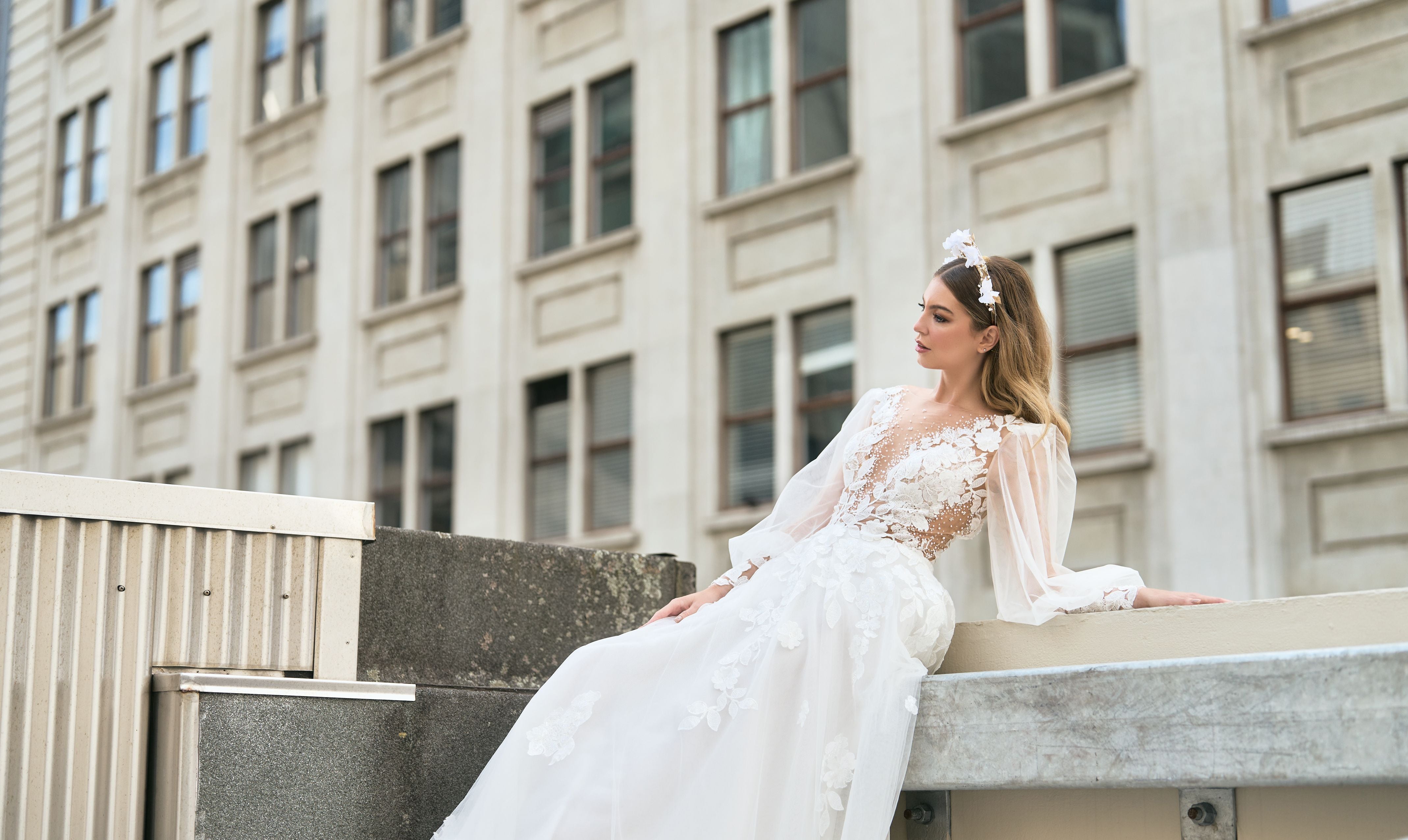 Rubi wedding dress with floral detailing on décolletage and skirt. Sheer sleeves add a delicate touch. Plunging v-neckline and A-line silhouette create an elegant and romantic look that makes you appear to be floating down the aisle.