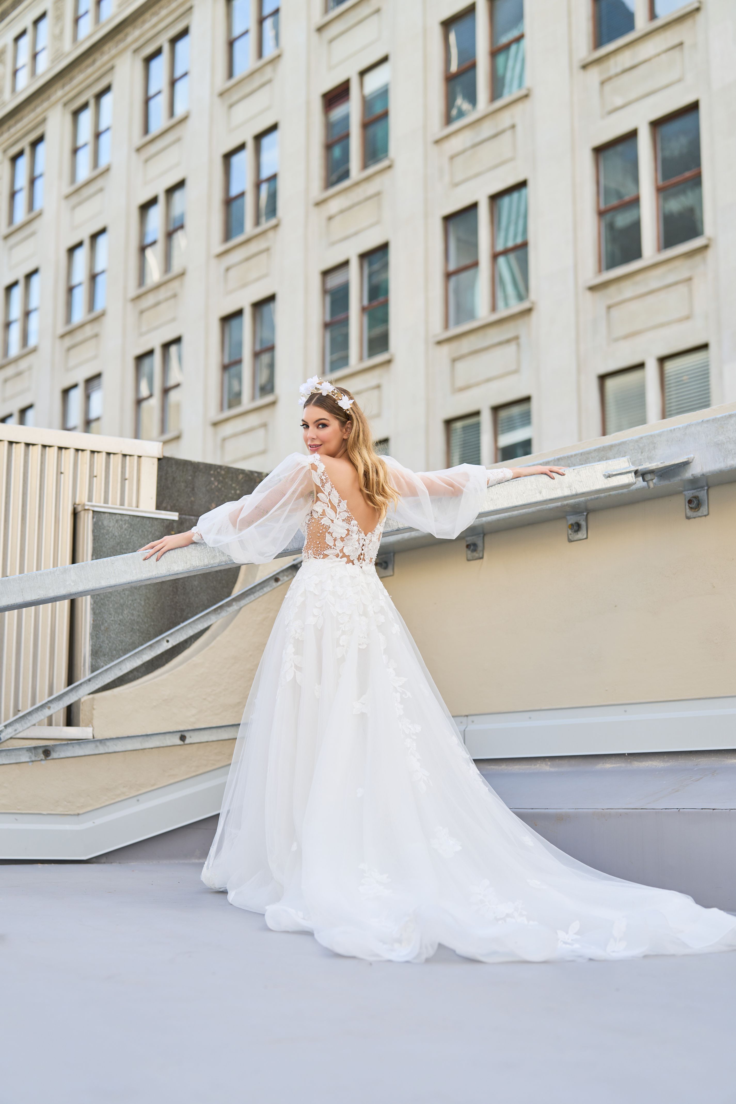 Wedding dress with floral detailing down plunging back and skirt. Sheer sleeves add a delicate touch. Plunging v-neckline and A-line silhouette create an elegant and romantic look that makes you appear to be floating down the aisle.