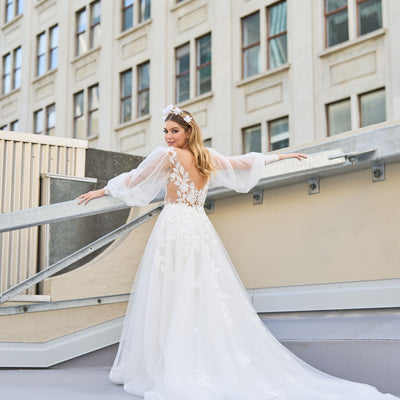 Wedding dress with floral detailing down plunging back and skirt. Sheer sleeves add a delicate touch. Plunging v-neckline and A-line silhouette create an elegant and romantic look that makes you appear to be floating down the aisle.
